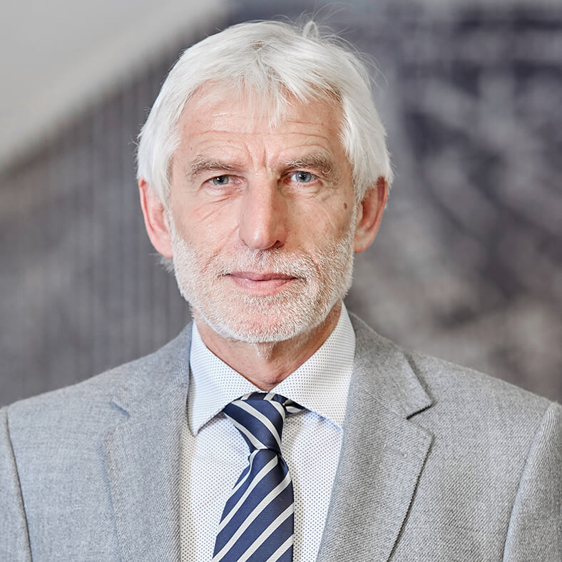 Porträt von Dr. Bernhard Ascherl. Er hat kurze, weiße Haare und einen Vollbart, trägt einen hellen Anzug mit hellem Hemd und dunkler Krawatte.