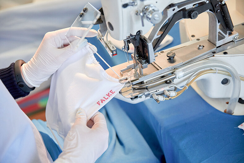 Die Maskenproduktion reichte nicht, um die Umsatzrückgänge zu kompensieren. Frauenhände in Handschuhen nähen einen Mund-Nasen-Schutz an einer Nähmaschine.