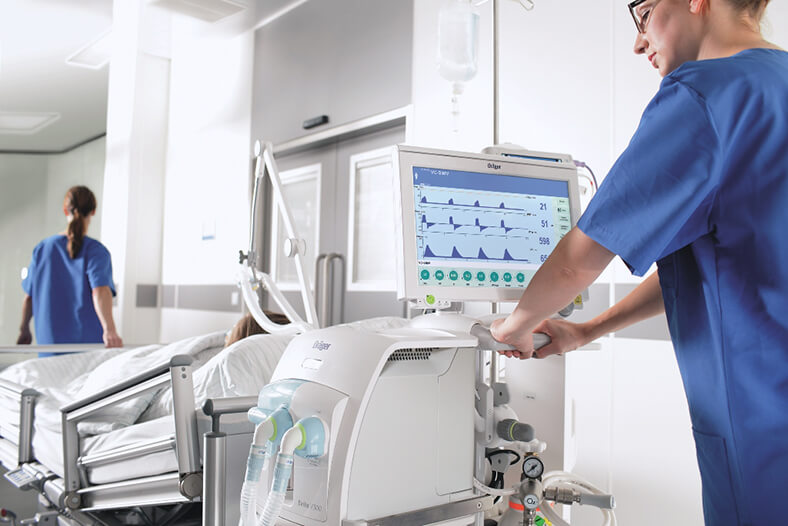 Ein Mann in Krankenhauskleidung steht an einem medizintechnischen Gerät hinter einem Krankenbett.