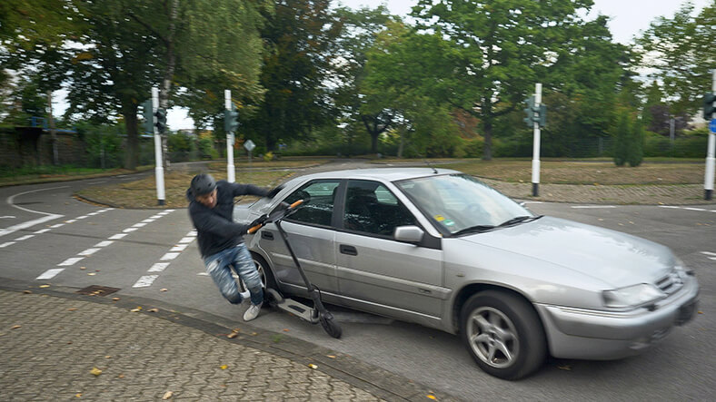 Das Foto zeigt ein Auto, das beim Abbiegen an einer Kreuzung einen E-Scooter schneidet und dessen Sturz verursacht.
