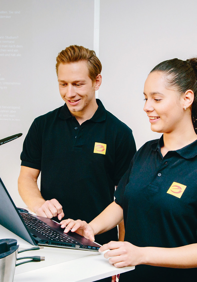 Die Elektrohandwerke kommen weiterhin relativ gut durch die Krise. Zwei Kollegen, Mann und Frau, in dunklen T-Shirts, schauen beide auf ein Notebook an einem Stehcounter.