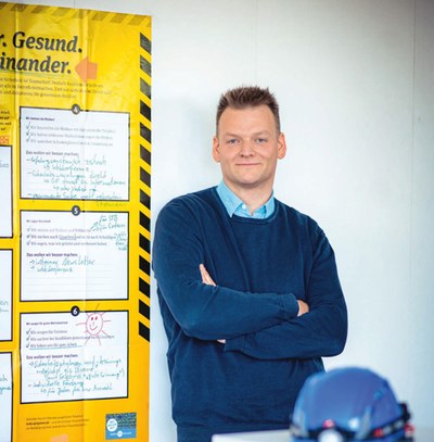 Halbkörper-Porträt von Raiko Schmidt, im Hintergrund an der Wand hängt das gelbe Risikoposter der BG ETEM.