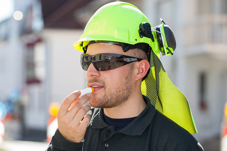 Mann mit gelbem Schutzhelm und Sonnebrille trägt UV-Schutz auf die Lippen auf.