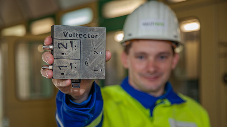 3. Westnetz GmbH, Dortmund: Voltector – zwei Mitarbeiter in Schutzkleidung und -helmen schauen zusammen auf ein kleines Gerät.