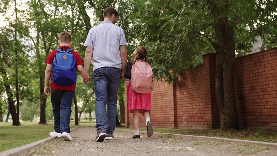 Vater mit zwei Schulkindern – ein Junge und ein Mädchen – an der Hand