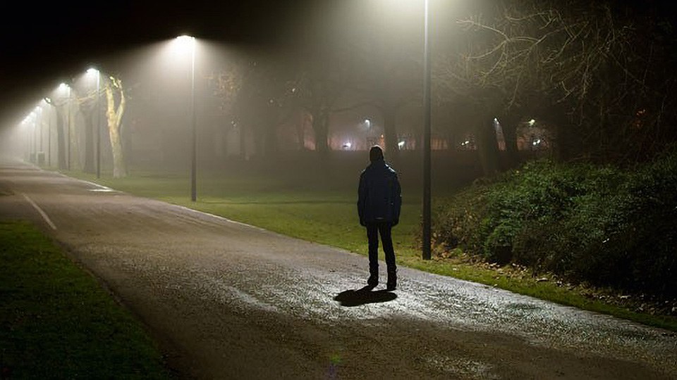 Einzelperson, die in der dunklen Nacht auf der schlecht beleuchteten Straße geht