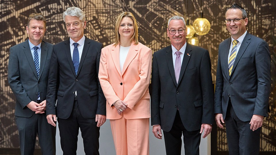 Fünf Personen stehend im Gruppenbild, in der Mitte eine Frau