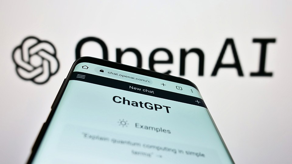 Blick auf Smartphone mit geöffneter Chat GPT App, darüber Schriftzug OpenAI