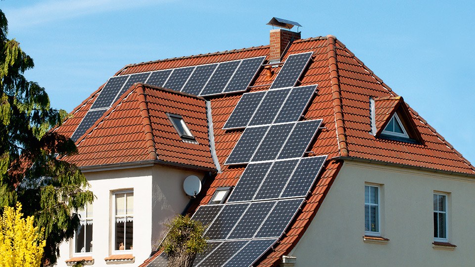 Blick auf oberen Bereich eines renoviertes Mehrfamilienhauses mit Solarpaneelen auf dem Satteldach