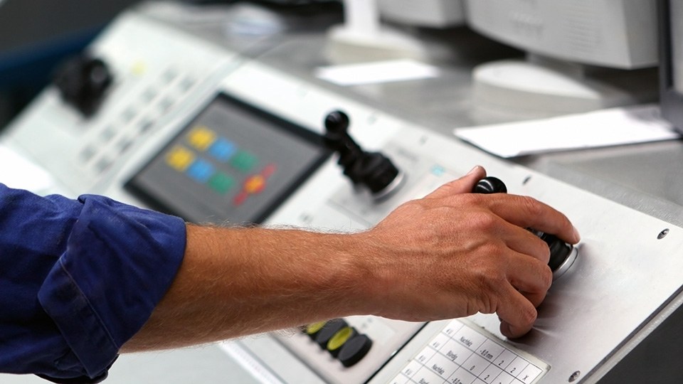 Eine Hand an einem Schaltpult bei der Bedienung einer Druckmaschine