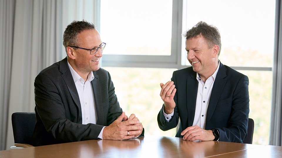 Marco Wetzel und Jörg Botti sitzen gut gelaunt im Gespräch an einem Tisch