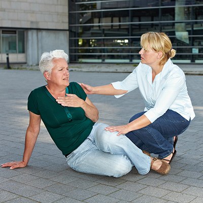 Passantin hilft einer Seniorin, die auf dem Boden sitzt und sich die Hand auf die Brust legt