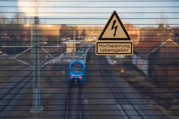 Aufnahme einer Bahntrasse mit einem Warnschild vor Hochspannung im Vordergrund