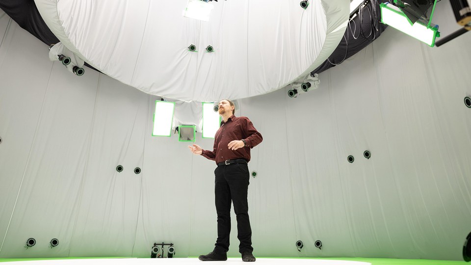 Ein Mann steht im Inneren eines Aufnahmestudios, das aussieht wie das Innere eines großen runden Zeltes, das mit Kameras versehen ist