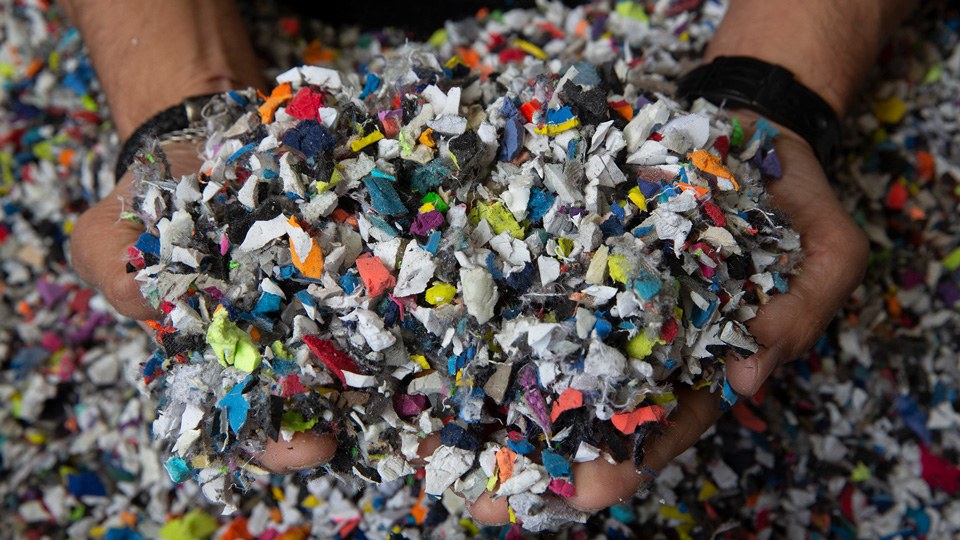 Nahaufnahme zweier Hände mit bunten, zerkleinerten Textil- und Materialresten aus dem Recyclingprozess von Alttextilien und Schuhen